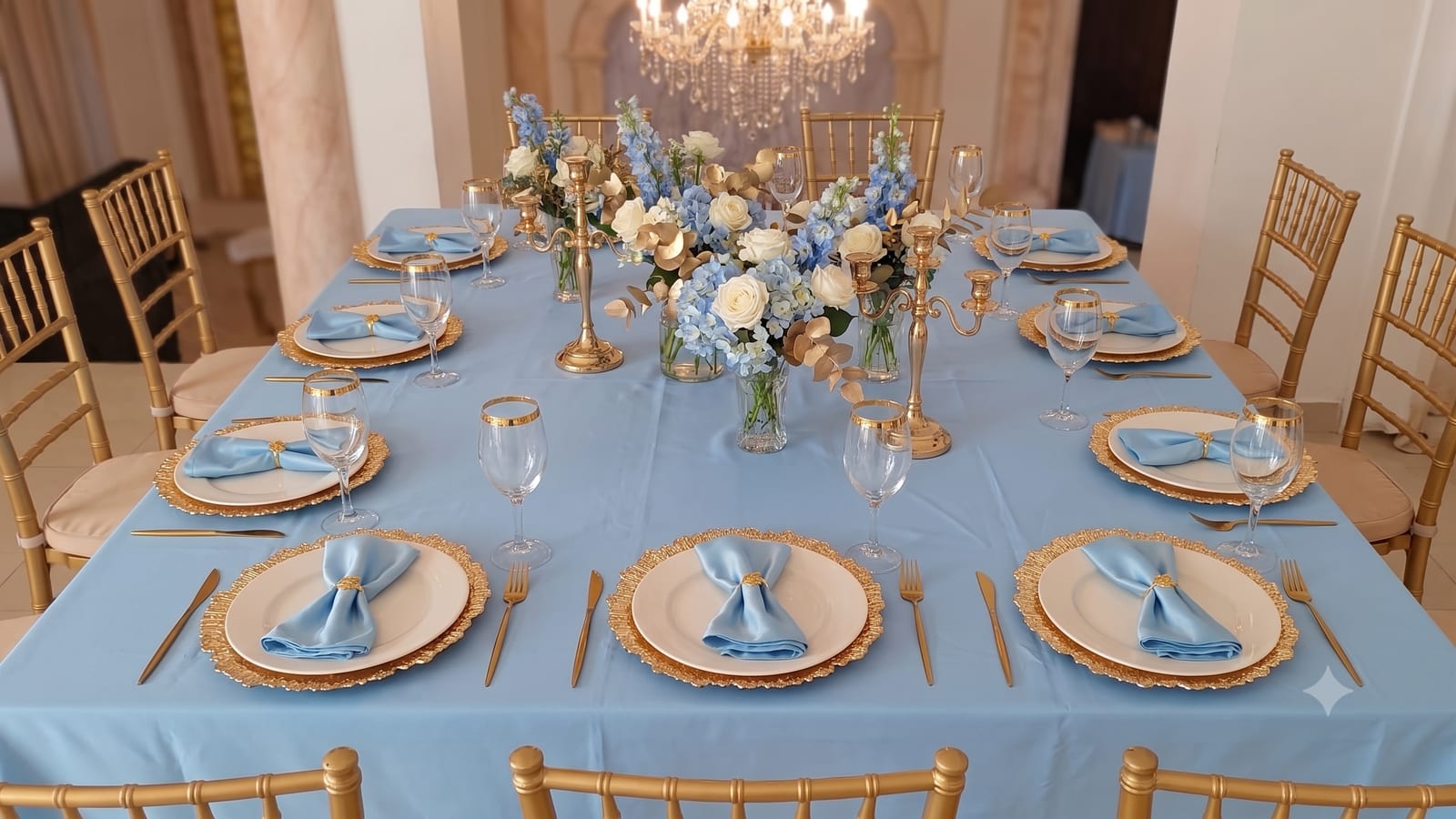Mesa de gala con mantel azul, platos base dorados, copas y candelabros para eventos